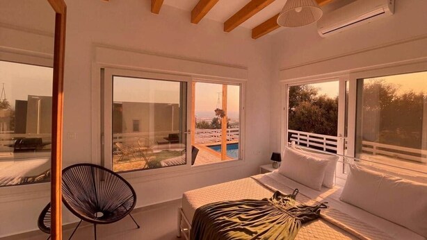 Un dormitorio con cama, una silla y ventanas amplias con vistas a una piscina y zona exterior.