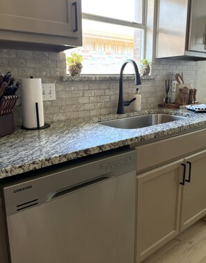 A kitchen with a granite countertop, stainless steel sink, and a Samsung dishwasher. - New Cozy Full House near ATT FIFA World Cup (Grand Prairie)