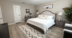 Une chambre à coucher comprenant un lit, des tables de chevet, une commode, une porte et une lampe fixée au mur.