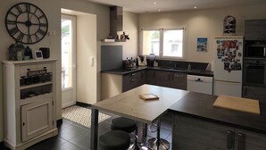 A modern kitchen with a large clock, a dining table, and a refrigerator. - Country house (Saint-Sylvestre-sur-Lot)