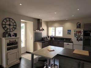 A modern kitchen with a large clock, a dining table, and a refrigerator. - Country house (Saint-Sylvestre-sur-Lot)