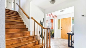 Eine Holztreppe mit Handlauf, eine Kakteepflanze und eine karierte Wanddekoration in einem Flur.