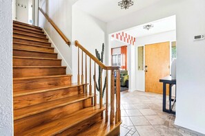 A wooden staircase with a handrail, a cactus plant, and a checkered wall decoration in a hallway. - Elegant Escape • Sleeps 14 • Games, Pool, Fire Pit (San Antonio)
