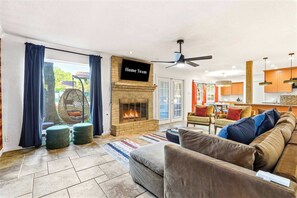 A living room with a fireplace, a sofa, a television, and a view of the outdoors. - Elegant Escape • Sleeps 14 • Games, Pool, Fire Pit (San Antonio)