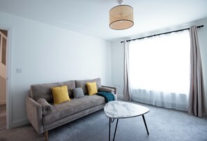 A modern living room with a sofa, a coffee table, and a large window with curtains. - Neptune House by Guestz (Chester)
