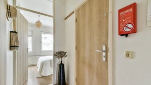 A hallway with a wooden door, a mirror, a vase with dried flowers, and a red sign with a no-smoking symbol.