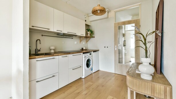 A compact kitchen with white cabinets, a wooden countertop, a washing machine, and a hanging light fixture.