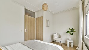 A bedroom with a bed, a chair, a potted plant, a hanging light fixture, and a window with curtains.
