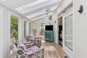 A sunlit room with a ceiling fan, a sofa, a cabinet, and a TV. - Captain's Quarters - Deep Water dock (St. Simons Island)