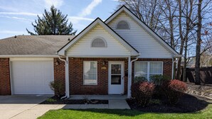 A single-story house with a garage, a front door, and a small front yard with shrubs. - Keystone Garden Villa G (Indianapolis)