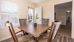A dining room with a wooden table and chairs, a door, and a window with blinds. - Keystone Garden Villa G (Indianapolis)