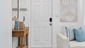 Una puerta blanca con manija, una consola de madera con cestas, un espejo y un interruptor de luz en la pared.