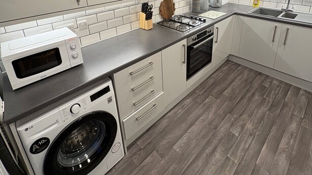 A modern kitchen with white cabinets, a built-in oven, microwave, and washing machine. - Park House Sleeps 4 With Enclosed Garden (Northampton)