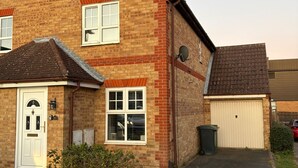 A two-story brick house with a white front door, two windows, a garage, and a satellite dish. - Park House Sleeps 4 With Enclosed Garden (Northampton)