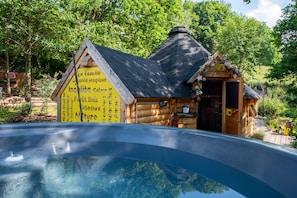 A wooden cabin with a signboard, a hot tub, and a natural surrounding.