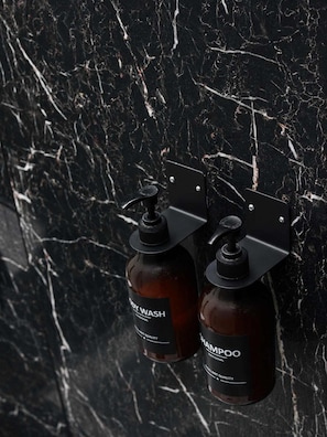 Zwei Flaschen Shampoo und Duschgel an einer schwarzen Marmorwand angebracht.