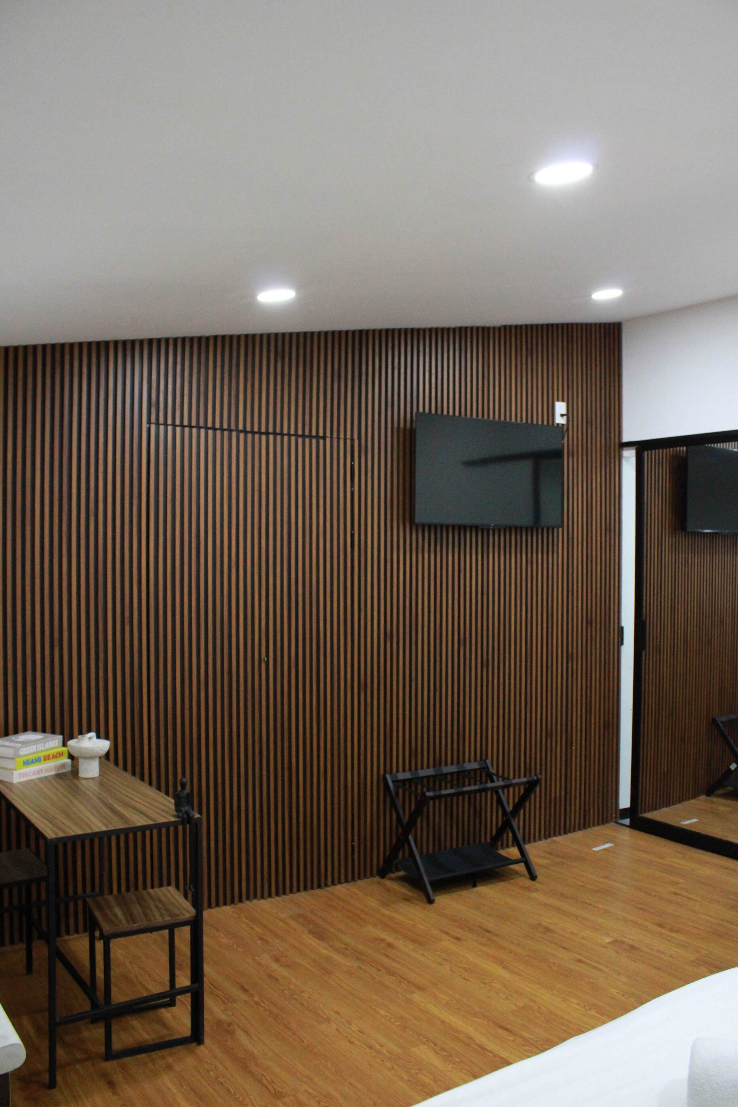 A modern room with a wooden panel wall, a flat-screen TV mounted above a black folding chair, and a wooden table with a few books.