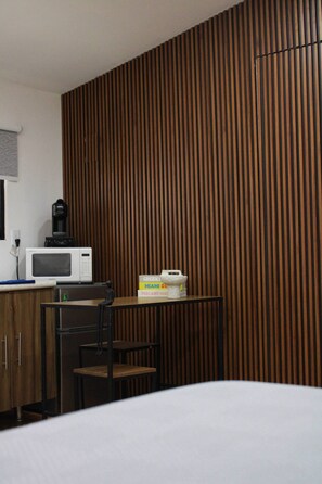 Ein Hotelzimmer mit einer Wand aus Holzlamellen, einer Küchenzeile mit Mikrowelle, einer Kaffeemaschine und einem kleinen Tisch mit einer weißen Schale.