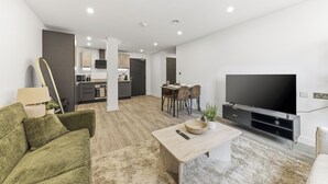 A modern living room with a sofa, coffee table, TV, and dining area. - Cosy Central York Apartment - Sleeps 4 - Free Gym (York)