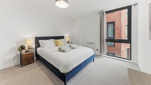 A bedroom with a bed, bedside tables, a lamp, a window with a view of a brick building, and a ceiling light. - Cosy Central York Apartment - Sleeps 4 - Free Gym (York)