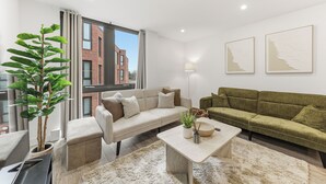 A modern living room with a beige sofa, a green sofa, a coffee table, a potted plant, and two wall art pieces. - Cosy Central York Apartment - Sleeps 4 - Free Gym (York)