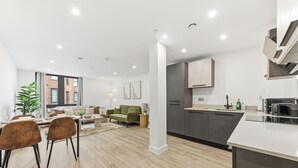 A modern kitchen with a central island, a dining area with chairs and a table, and a living room with a sofa and a coffee table. - Cosy Central York Apartment - Sleeps 4 - Free Gym (York)