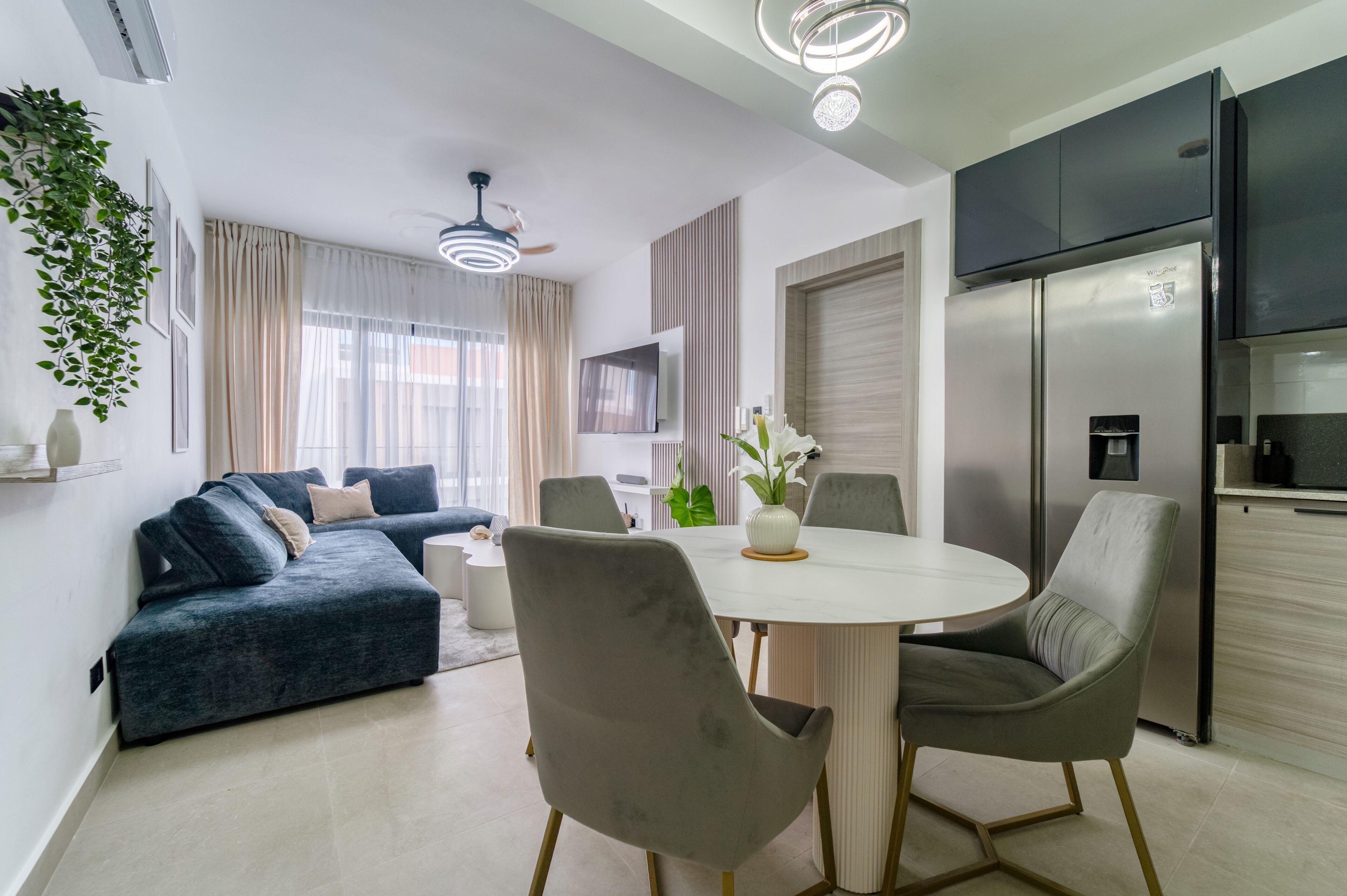 Uma sala de estar moderna com sofá, mesa de jantar, cadeiras, TV e cozinha.