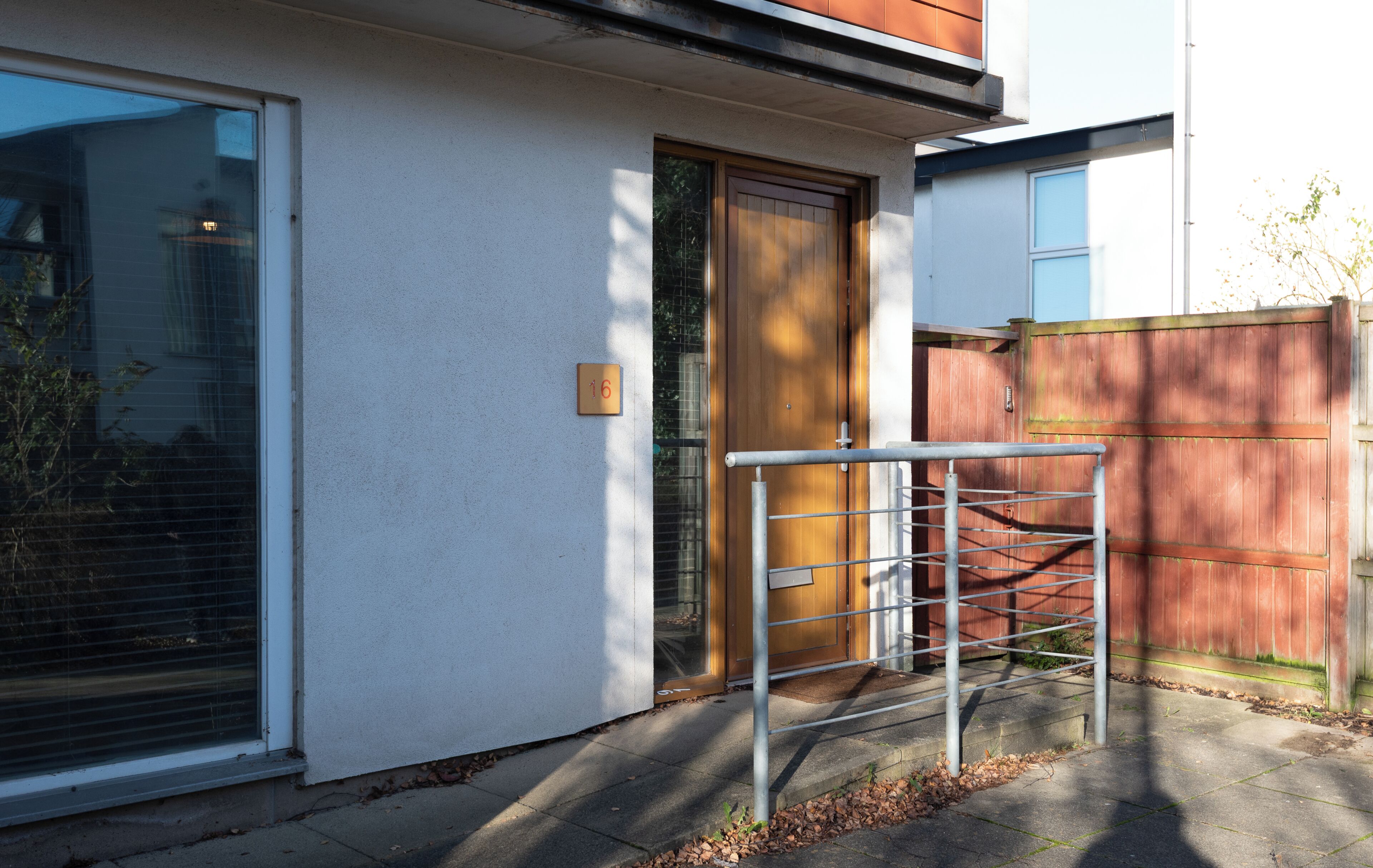 En bostadsbyggnad med en vit fasad, en trädörr och ett metallstaket.