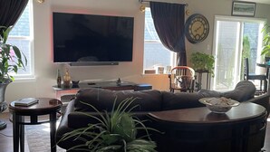 Ein Wohnzimmer mit großem Flachbildfernseher, einem dunkelgrauen Sofa, einem Couchtisch und einer Zimmerpflanze.
