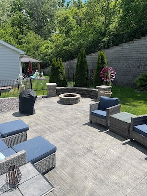A patio with outdoor furniture, a fire pit, and a garden with trees and a stone wall. - Home Retreat -Cozy Neighborhood, 2 bedroom, 3 full baths, 4 guests (O'Fallon)