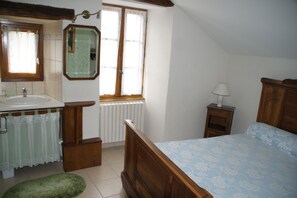 Ein Schlafzimmer mit Bett, Nachttisch, Lampe, Fenster, Heizkörper, Spiegel, Waschbecken und einem grünen Teppich.