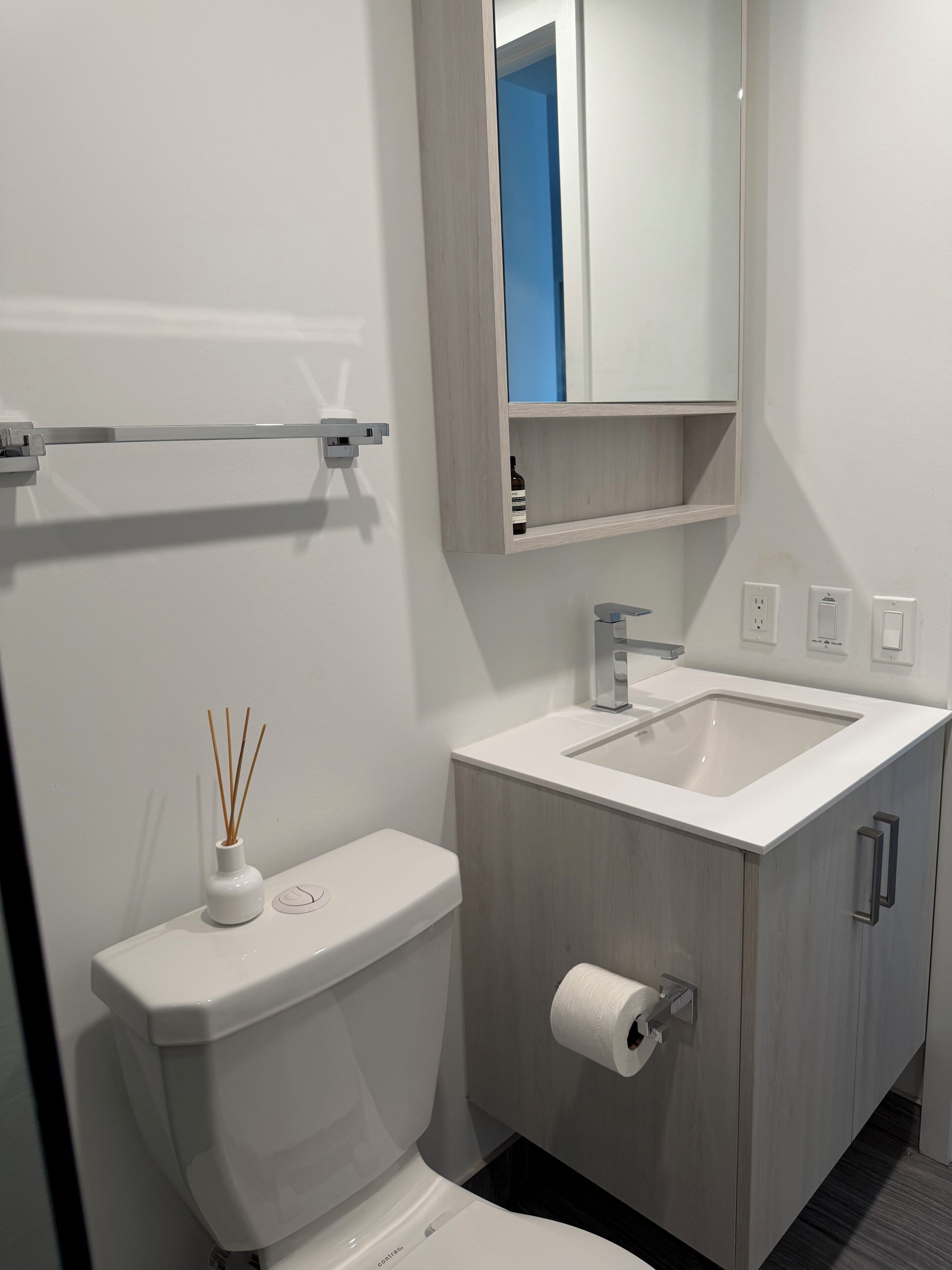 A modern bathroom with a toilet, sink, mirror, and towel rack.