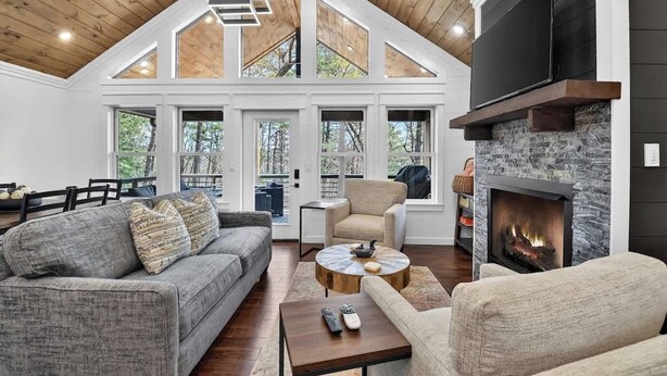 A spacious living room with a fireplace, a high ceiling with exposed beams, and large windows. - Stone's Throw | Hot Tub + Fire Pit + Easy Roads (Blue Ridge)