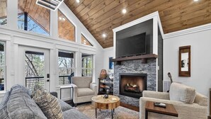 A modern living room with a fireplace, large windows, and a high ceiling. - Stone's Throw | Hot Tub + Fire Pit + Easy Roads (Blue Ridge)