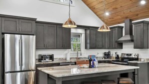 A modern kitchen with dark cabinets, stainless steel appliances, and a central island with stools. - Stone's Throw | Hot Tub + Fire Pit + Easy Roads (Blue Ridge)