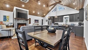 A spacious living area with a fireplace, a dining table with chairs, and a kitchen with modern appliances. - Stone's Throw | Hot Tub + Fire Pit + Easy Roads (Blue Ridge)