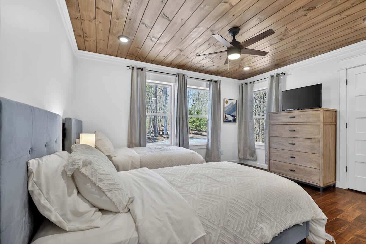 A bedroom with two beds, a ceiling fan, a TV, and a wooden dresser.