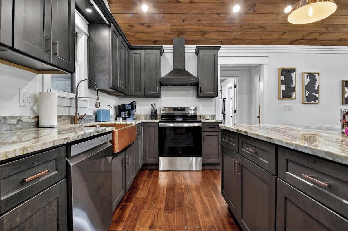 A modern kitchen with dark cabinets, stainless steel appliances, and a wooden ceiling.