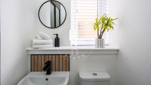 Een badkamer met een wastafel, toilet, een stapel handdoeken, spiegel en een potplant.