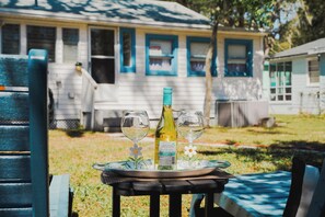 Ein Tisch mit einer Flasche und zwei Gläsern, ein Stuhl und ein Haus im Hintergrund.