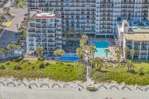 Ein Hochhaus-Hotel mit mehreren Balkonen, einem Swimmingpool und Strand.
