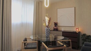 Ein moderner Essbereich mit einem runden Glastisch, zwei Stühlen, einer Blumenvase, einem an der Wand befestigten abstrakten Gemälde und einer Kerze auf einem Beistelltisch.