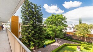 Ein Balkon mit Blick auf einen gepflegten Garten, darunter ein hoher Nadelbaum und ein ordentlich geschnittener Heckenstreifen.