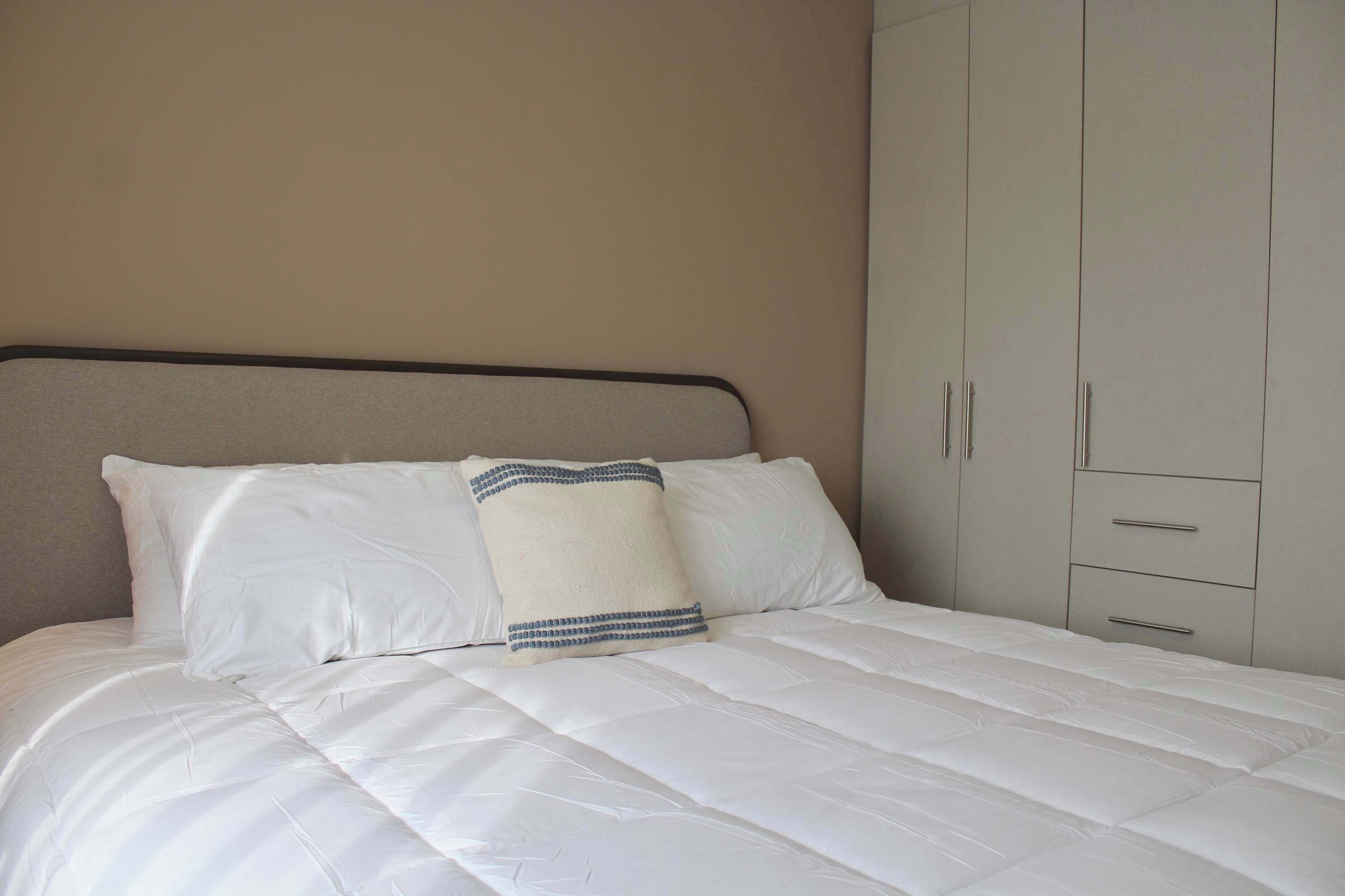 Una cama con ropa blanca, un cabecero y una almohada decorativa.