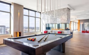 Une table de billard dans une pièce moderne, dotée de grandes fenêtres et offrant une vue sur la ville.