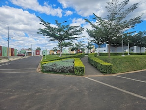 A residential street with houses, a clear sky, and a well-maintained hedge. - Mi casita relax 101-SV (Ahuachapán)