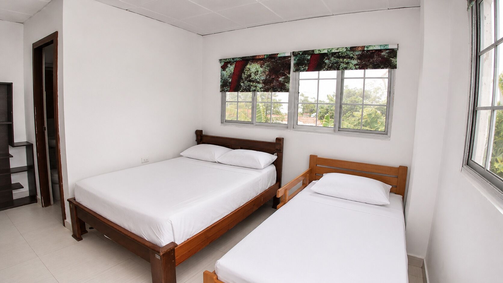 A bedroom with two wooden beds, a window with a view, and a door leading to another room.