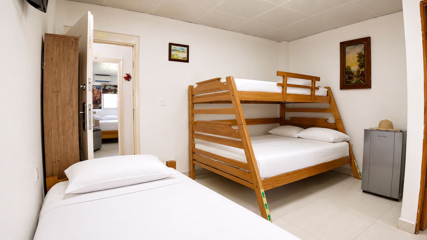 A bunk bed room with a wardrobe, a small cabinet, and two framed pictures on the wall.