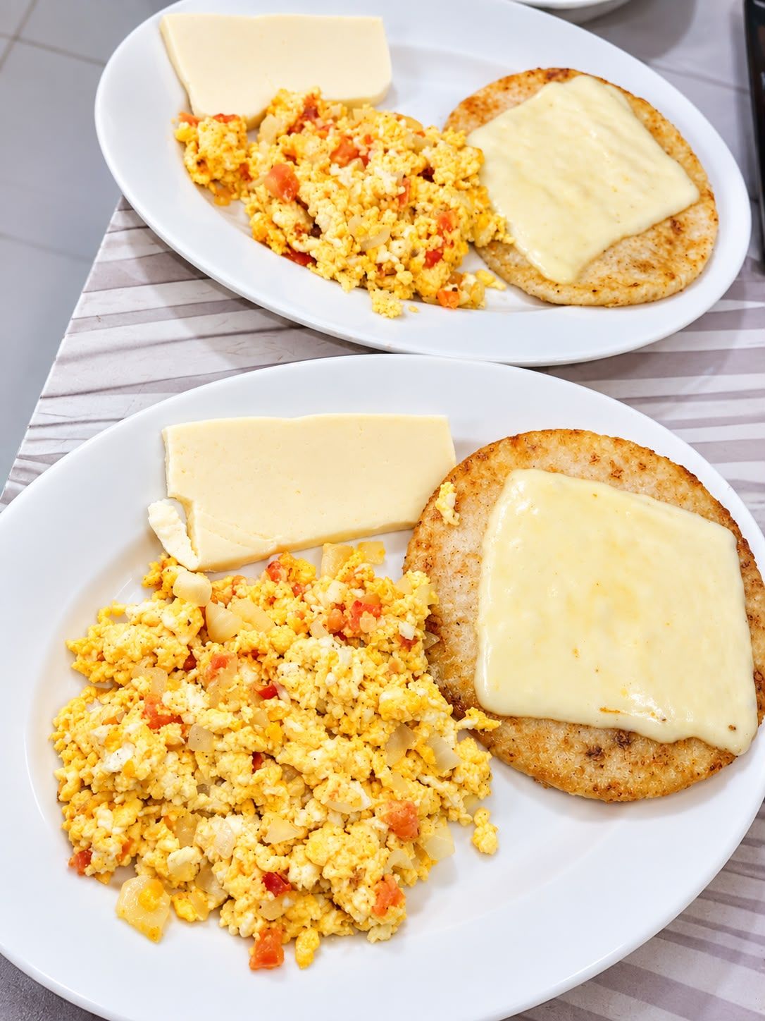 Dos platos de huevos revueltos con queso y tostadas.