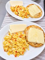 Dos platos de huevos revueltos con queso y tostadas.